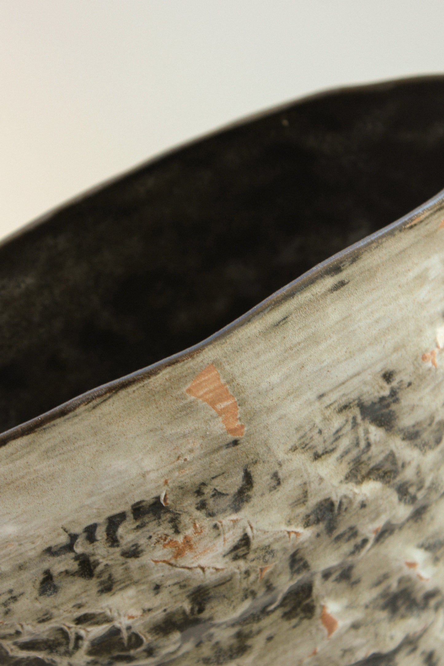 Close-up of a textured ceramic vase with a dark brown interior.