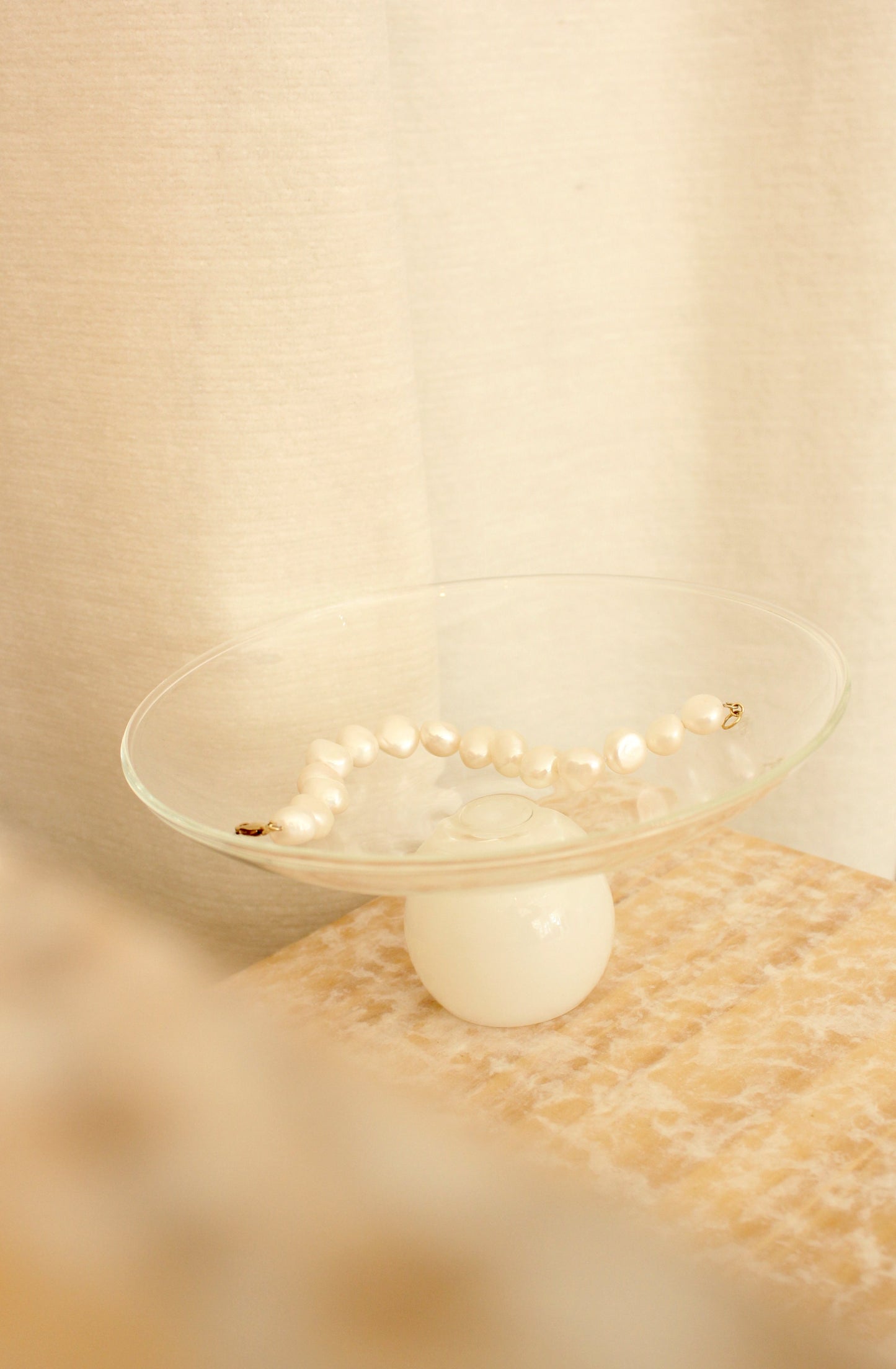 Pedestal glass bowl with clear top and white ball base, with pearl bracelet on top.