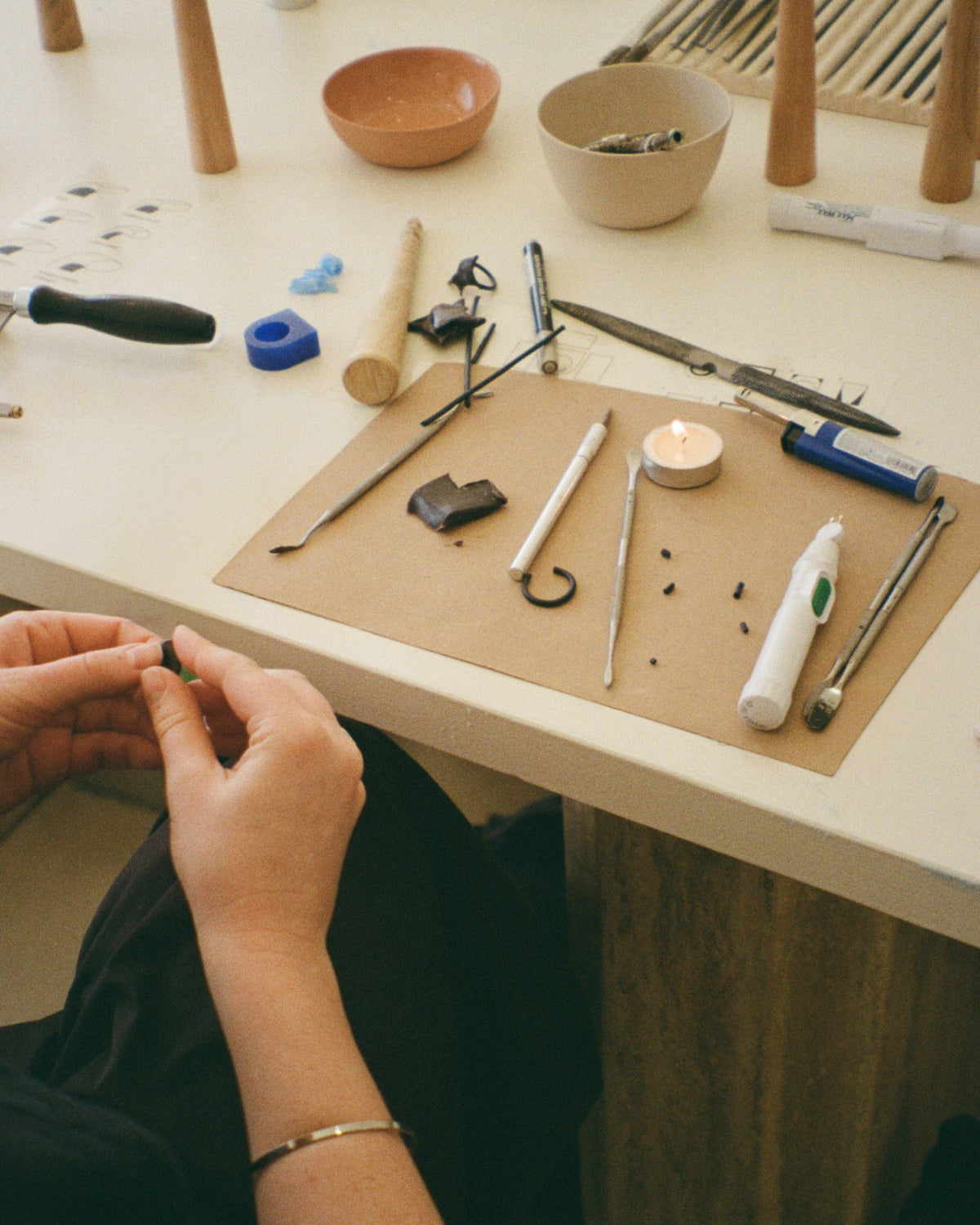 Workbench with jewelry-making tools and materials, including hands working on a piece of jewelry.