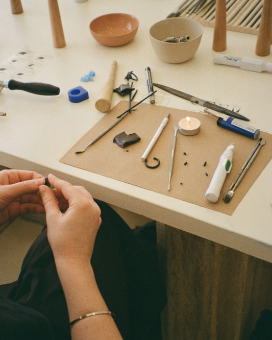 Workbench with jewelry-making tools and materials, including hands working on a piece of jewelry.
