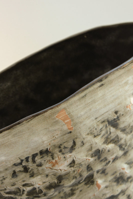 Close-up of a textured ceramic vase with a dark brown interior.