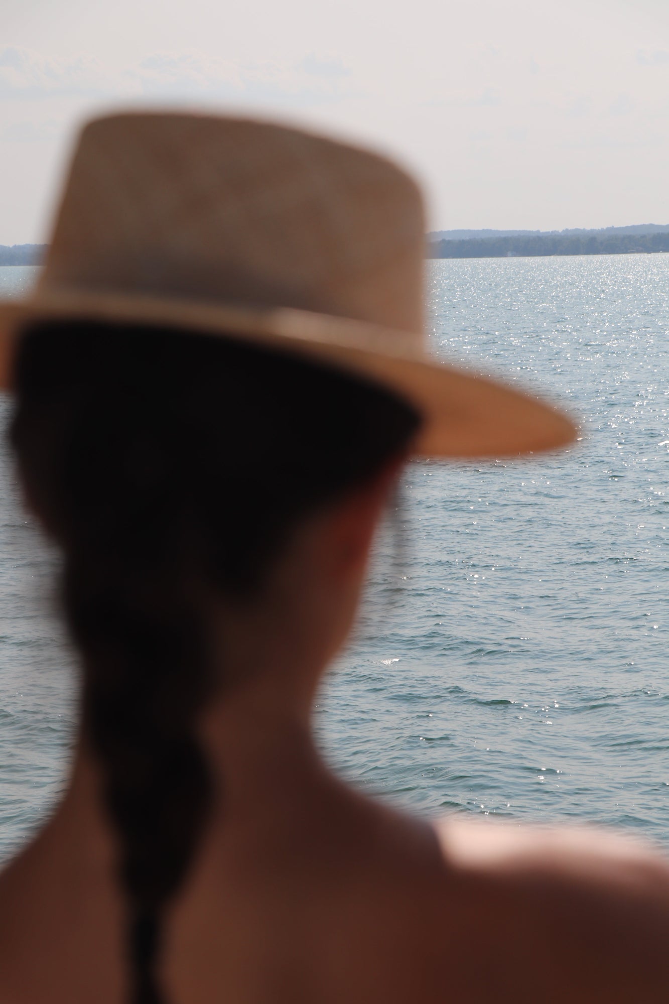 Blurred photo of woman wearing straw boater hat with lake in the background.
