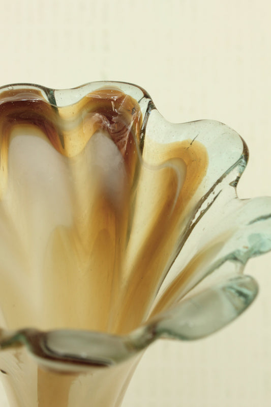 Multi colour glass flower shaped vase with wavy edges on a beige background.